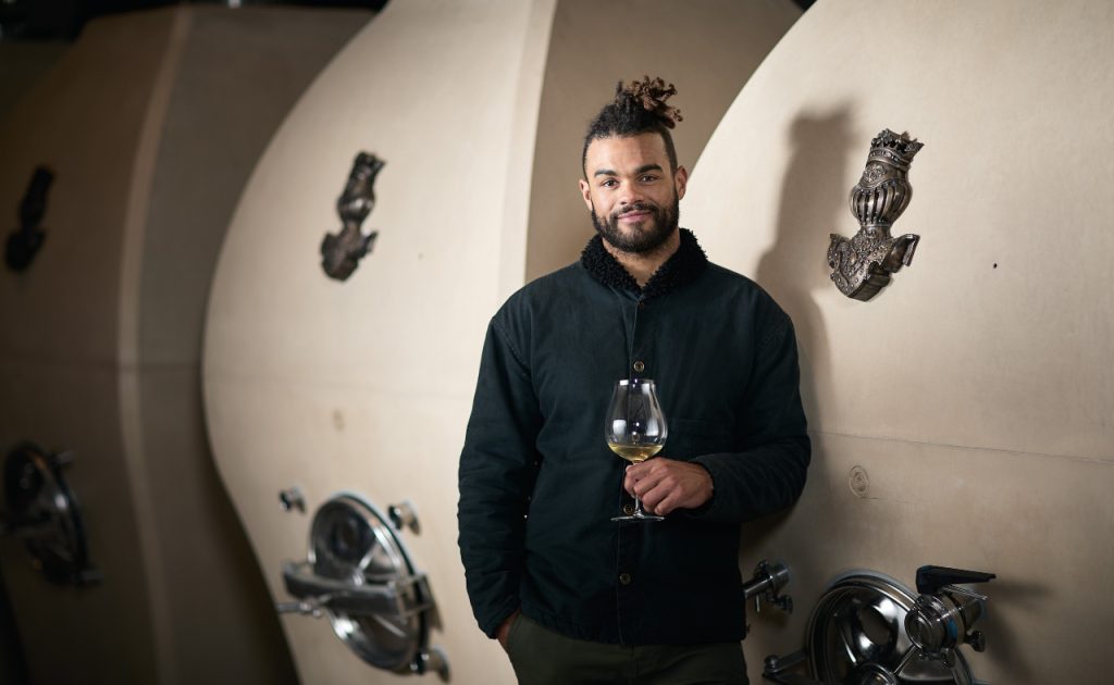 Knights Bridge Winery Winemaker Derek Baljeu next to concrete Tanks with Bronze Knight’s Head Emblems. 