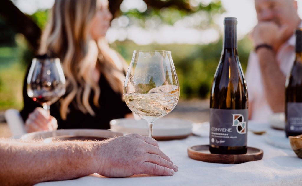 Convene Pinot Noir and Chardonnay wines on table with people.